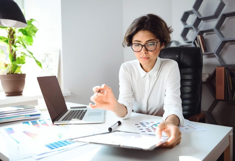 Young beautiful businesswoman in glasses sitting at workplace in office.